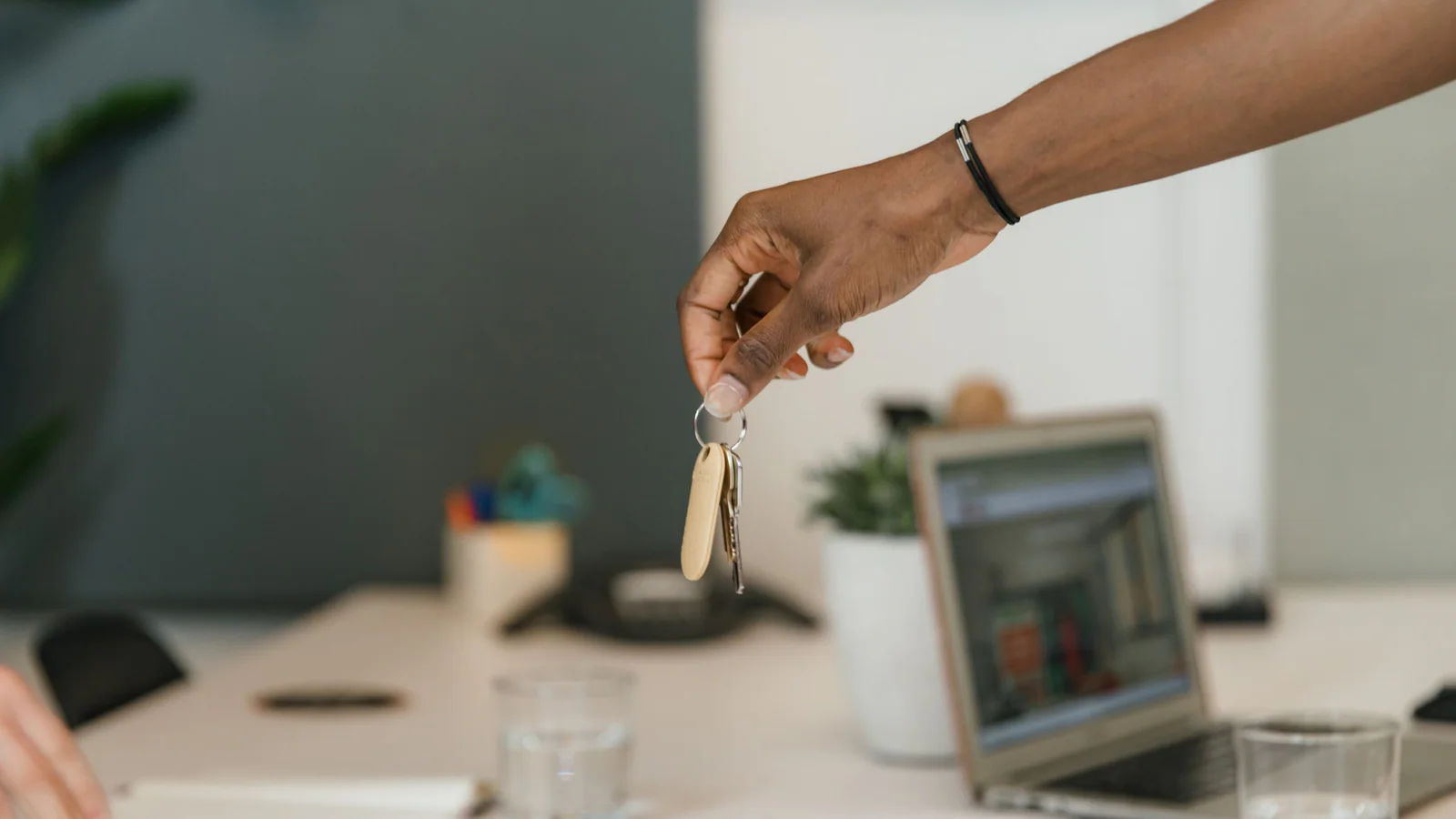 Hand holding keys above a desk and laptop