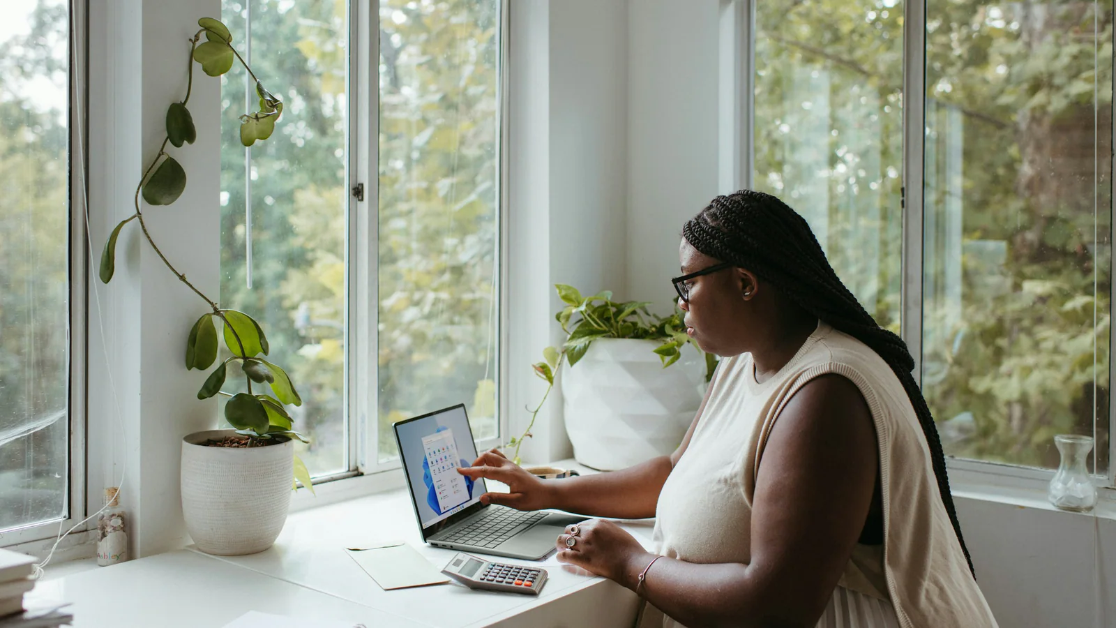 Woman using a calculator beside a laptop at a home desk
