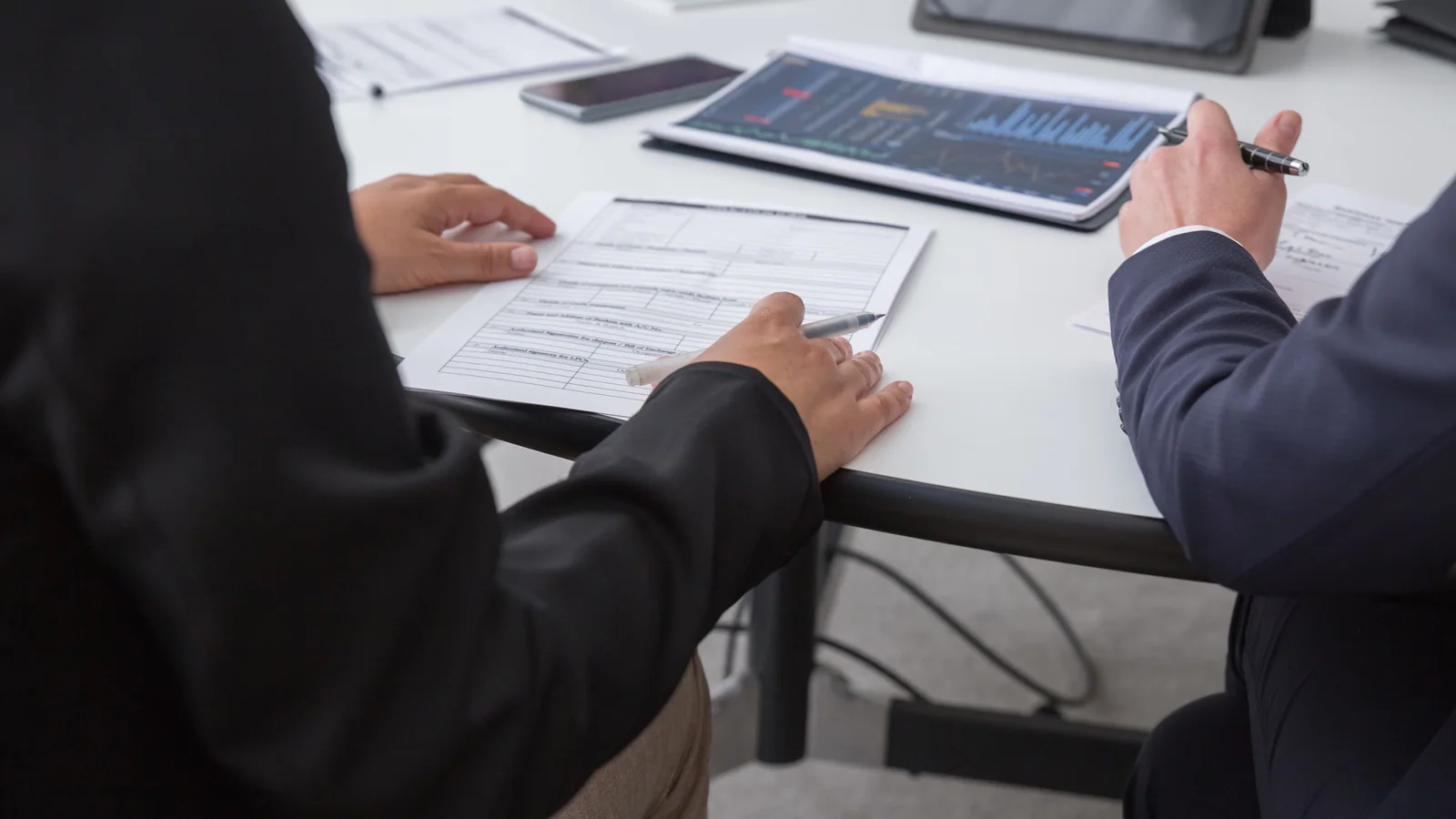 Two professionals reviewing documents and data at an office table