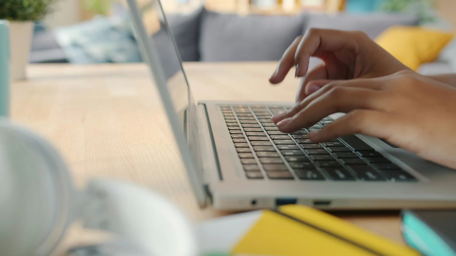 Hands typing on a laptop at a bright home-office desk