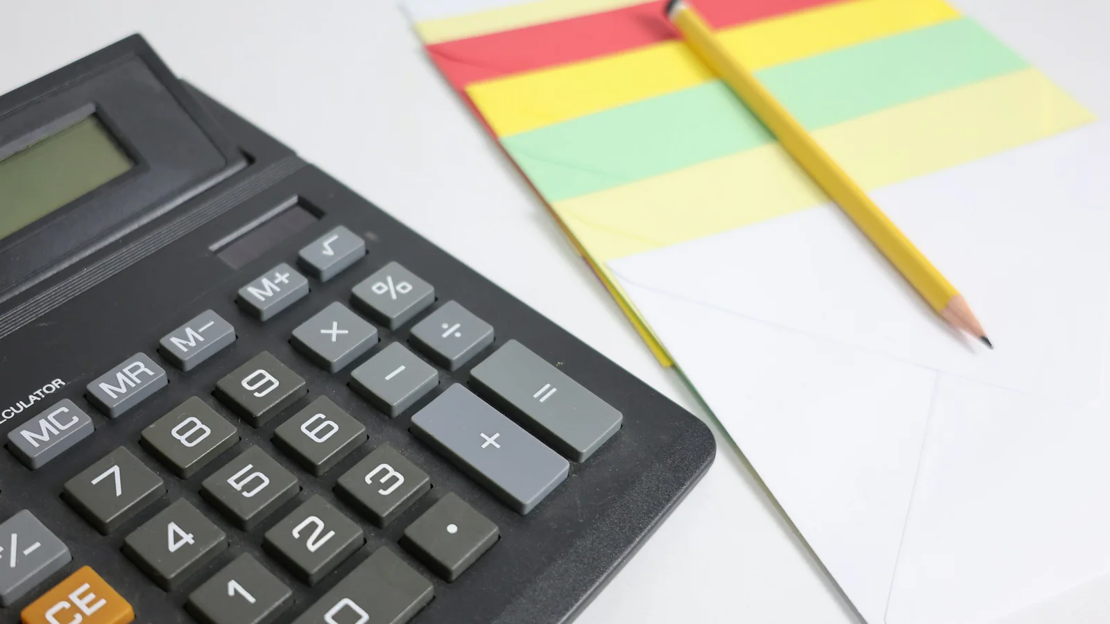Calculator beside blank paper and a pencil