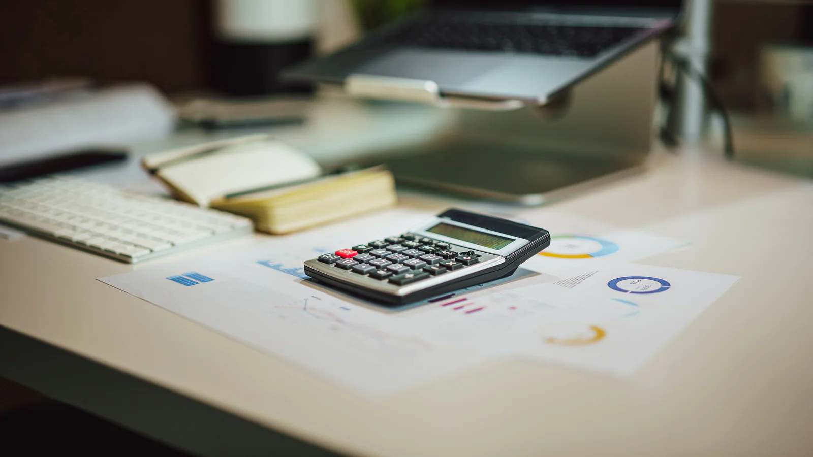 Calculator on financial papers beside a laptop