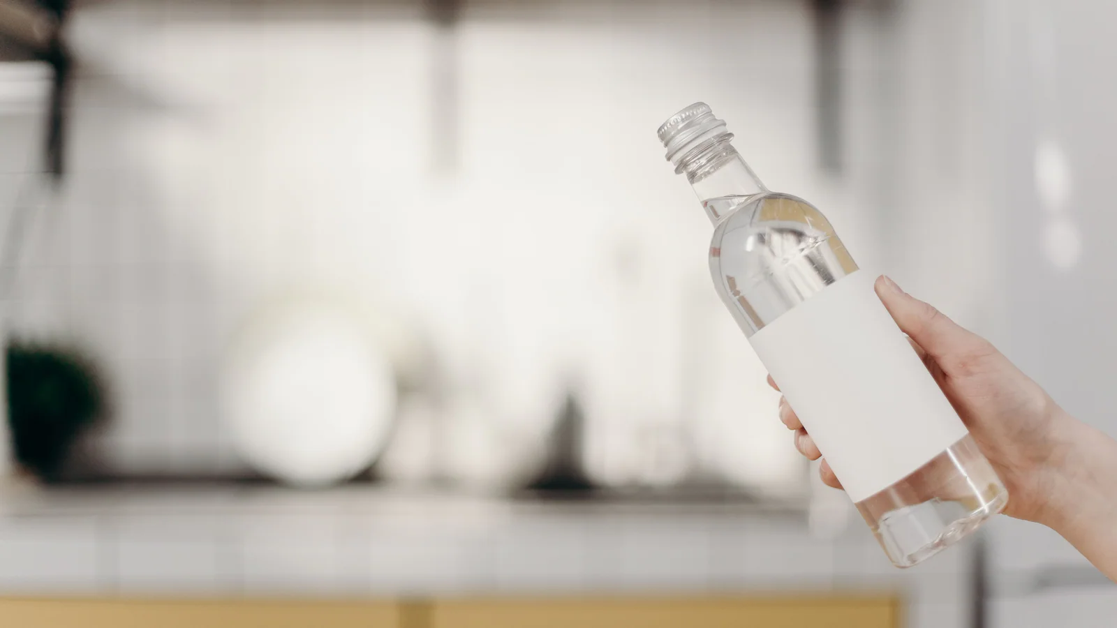 Hand holding a clear bottle with a blank white label