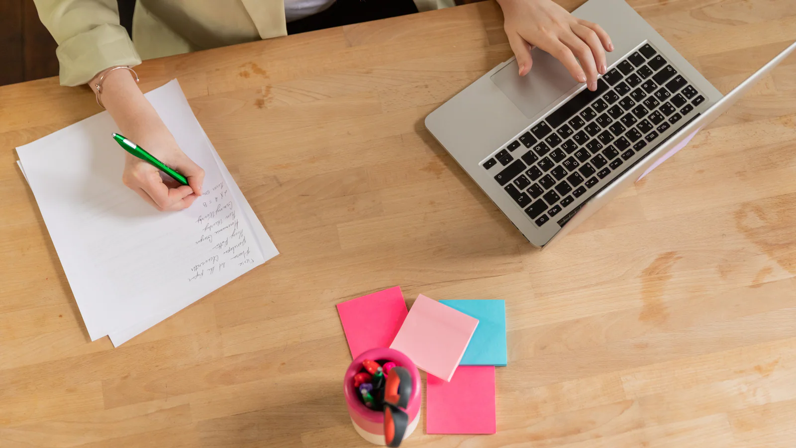 Person organising handwritten notes beside a laptop