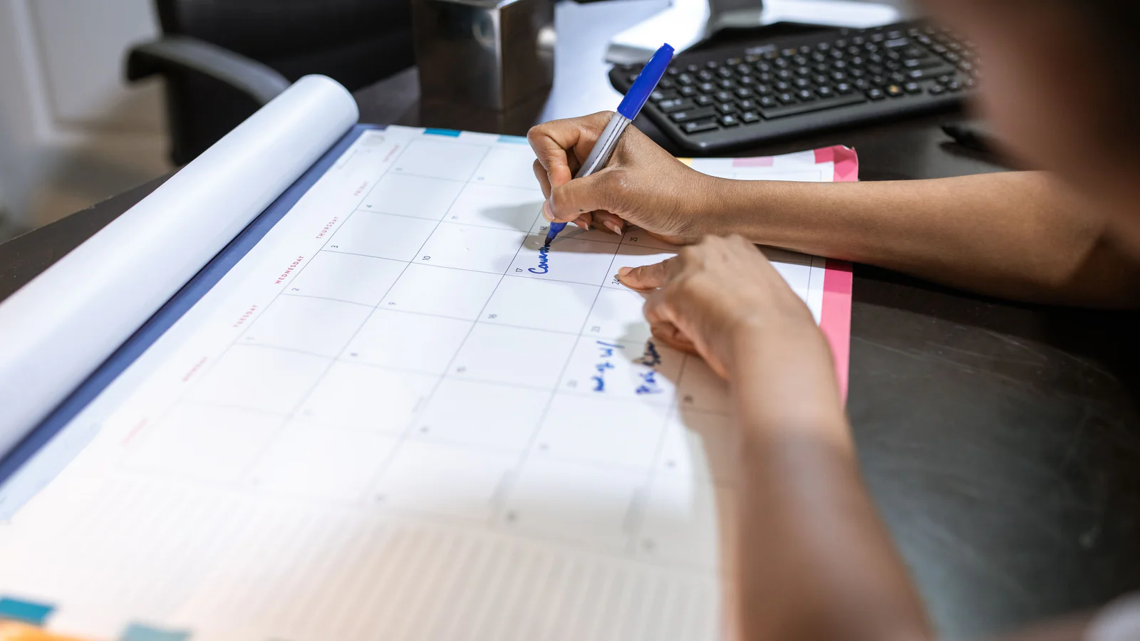 Person marking a paper calendar beside documents at an office desk