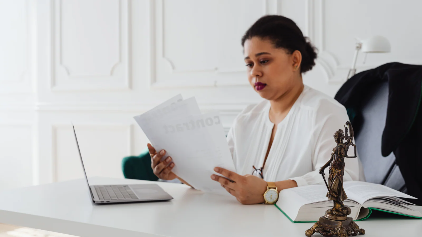 Professional reviewing documents at a desk beside an open book and laptop
