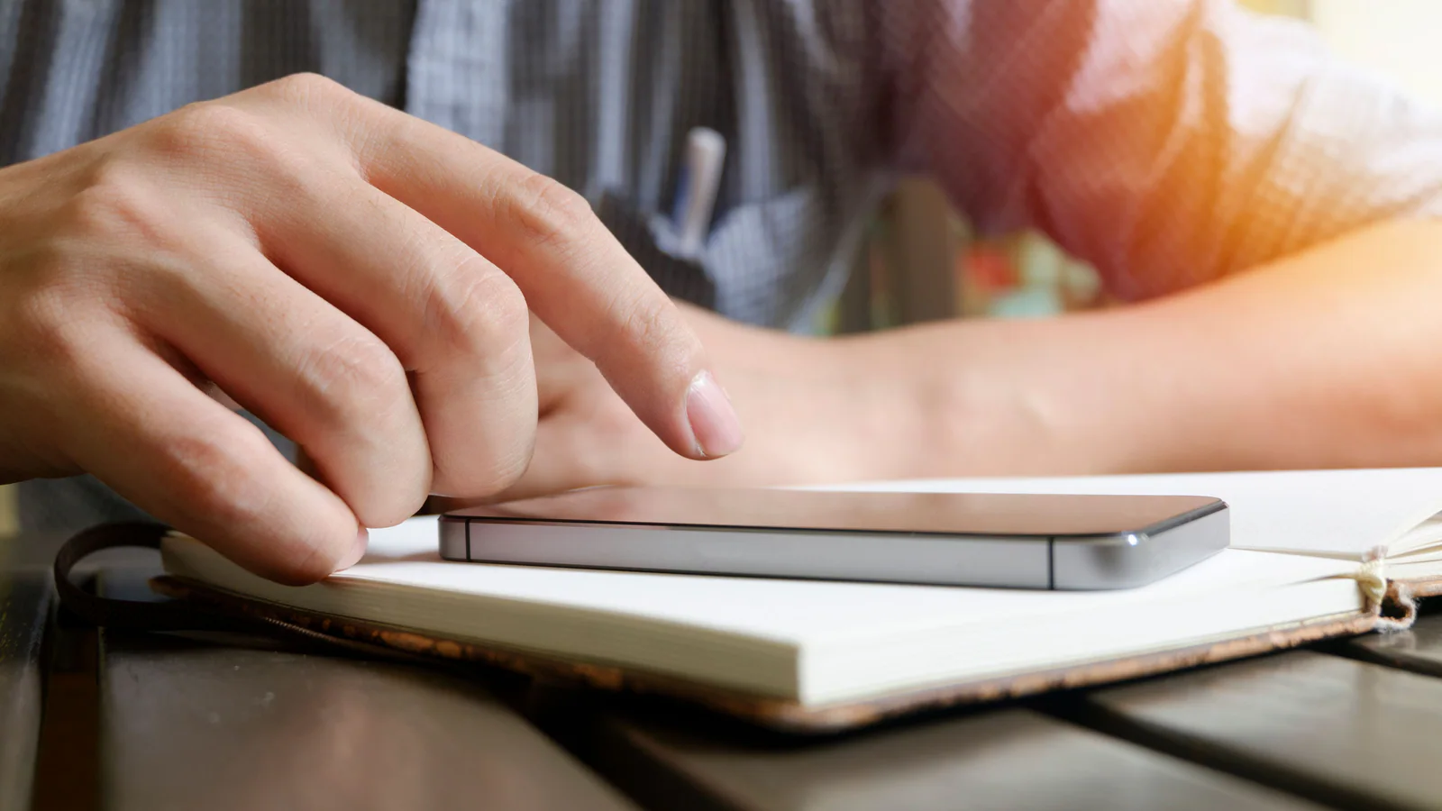 Person using a smartphone beside a notebook