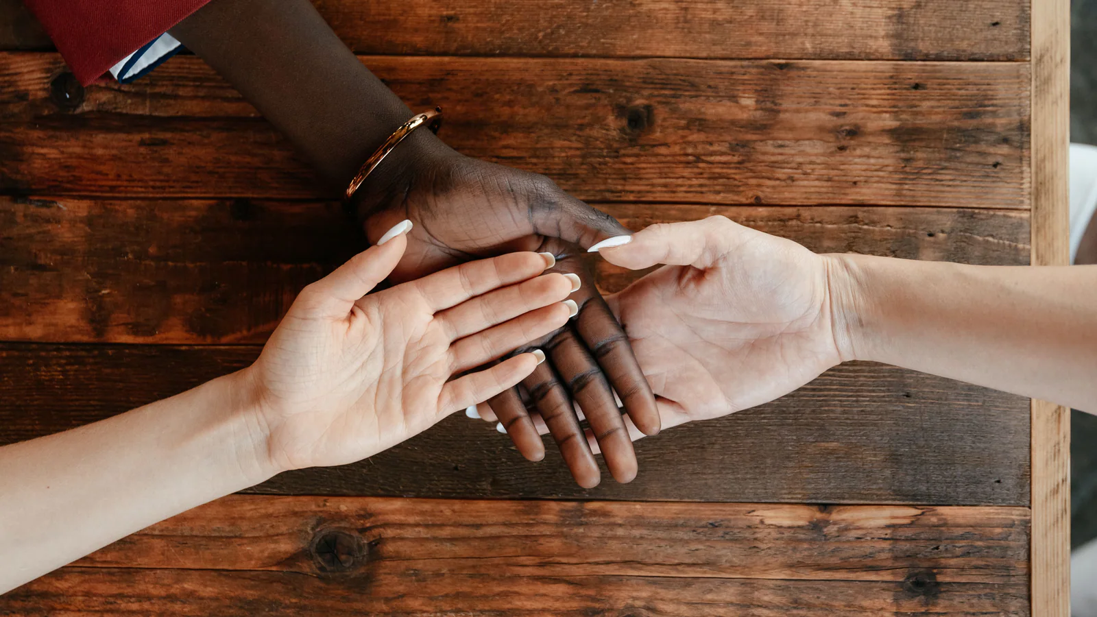Three anonymous hands meeting above a wooden table