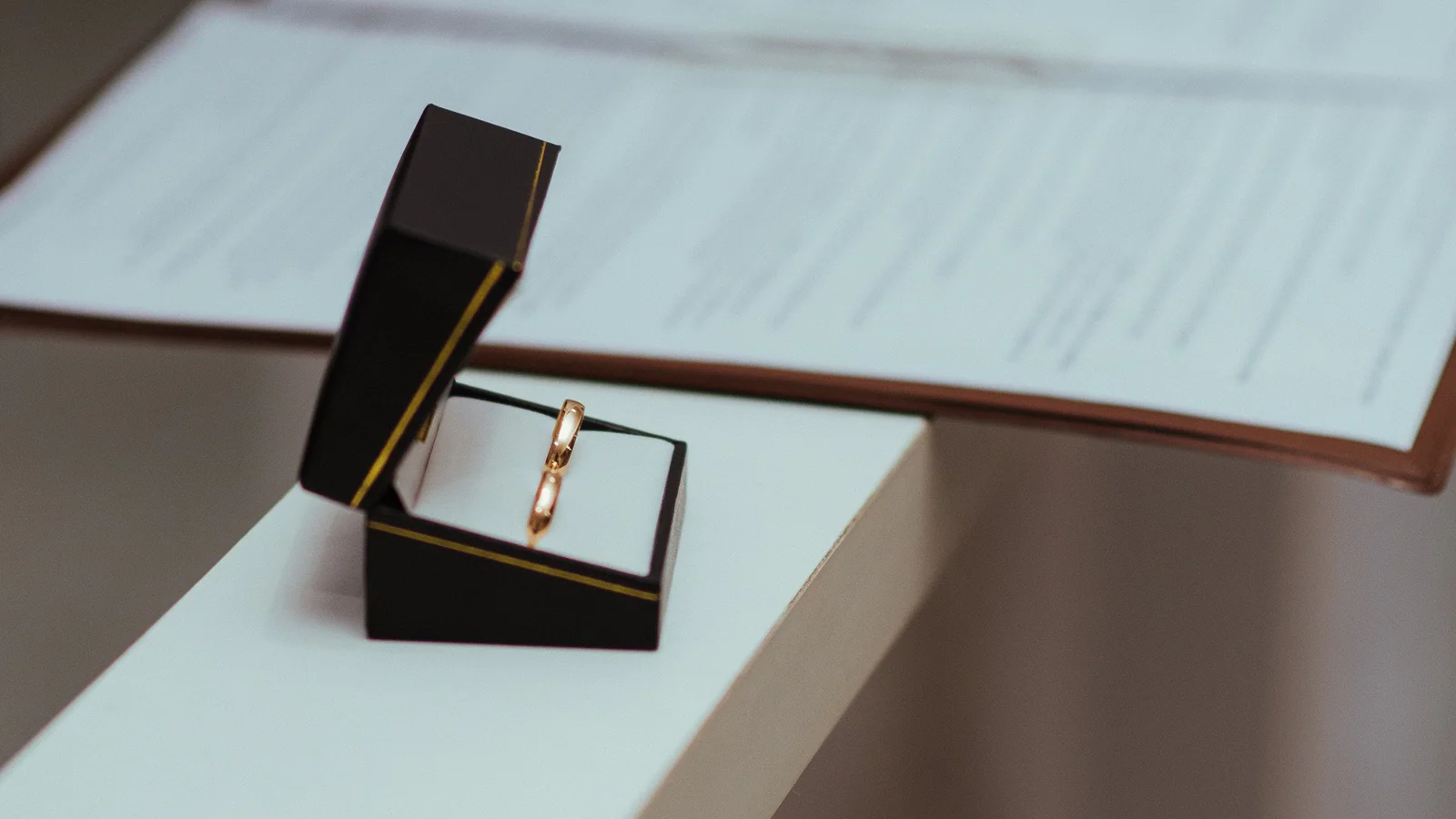 Two wedding bands in an open box beside blurred documents
