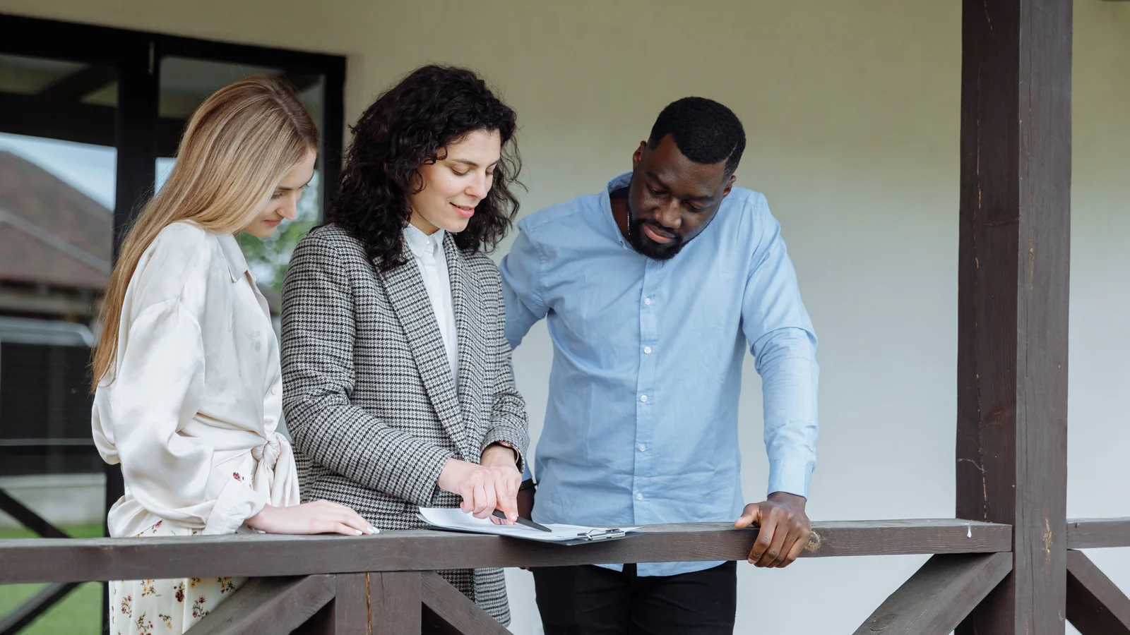 Three adults reviewing a document outside a house